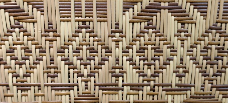 A close-up of a traditional two-tone woven bamboo or split-rotan mat featuring a geometric kelarai or basket-weave pattern with alternating light cream and dark brown strands.