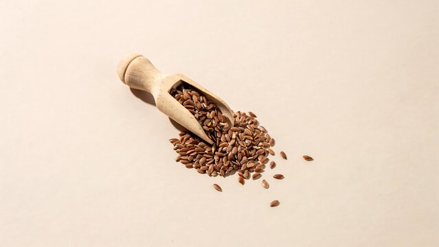 Wooden scoop with flaxseeds spilling on light background