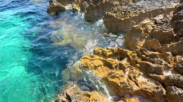 Turquoise Sea Waves on Rocky Coast. Clear turquoise sea water moving along a rocky coastline on a sunny day.