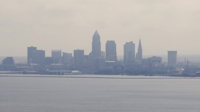 Cleveland, OH skyline with cloudy moody sky above on overcast summer day as tall buildings, skyscrapers, office building, and structures in silhouette stand over Lake Erie on Ohio coastline 4k