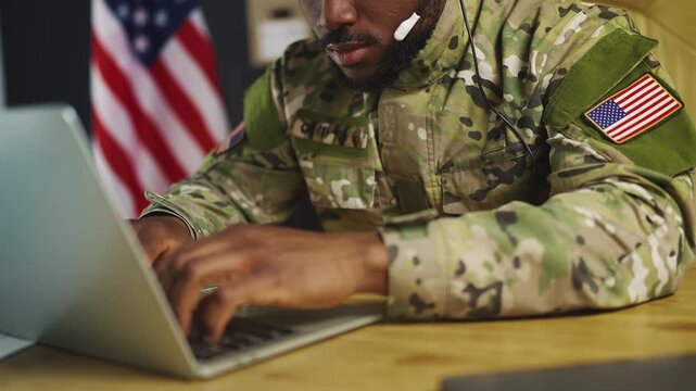 African American serviceman in headset tracks hostile activity using laptop