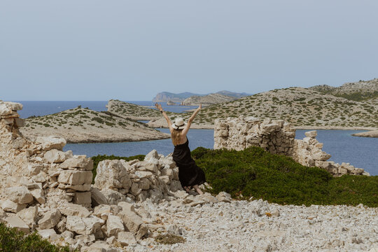 Woman in a black dress enjoying the scenic Adriatic coast among ancient stone ruins in Kornati, Croatia, surrounded by rocky islands, clear water and Mediterranean nature.