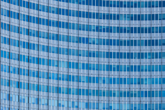 Blue glass wraps a curved facade as windows form a continuous grid, where repetition turns modern architecture into a cool geometric pattern.