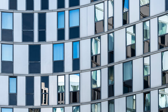 A curved glass facade layers windows and reflection across blue and silver panels, turning a precise grid into a flowing pattern of modern architecture.