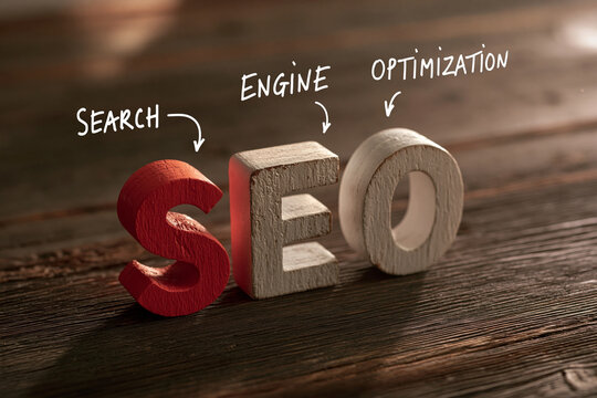 Three-dimensional wooden letters spelling "SEO" with corresponding 'Search Engine Optimization' text on a dark wooden surface. Represents digital marketing and web optimization.