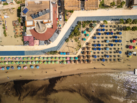 Albania, Durres 07 09 2025: Top-down aerial photo showing layers of shallow sea, sandy shoreline, colorful beach umbrella rows, promenade, and Hotel Restorant Kosova.