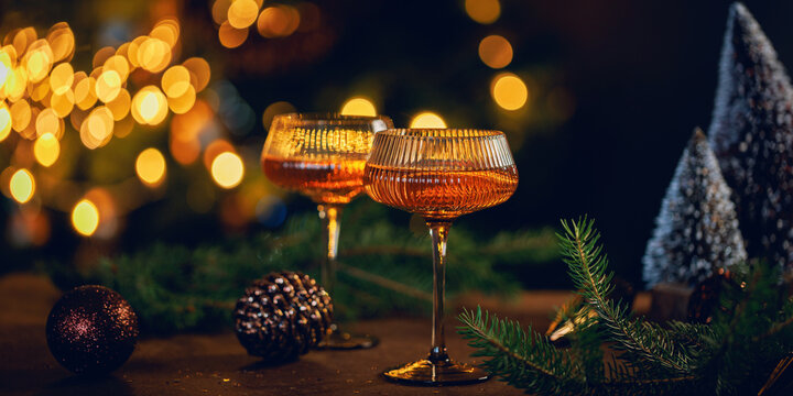 Stylish coupe glasses with sparkling rose wine on a festive holiday table surrounded by evergreen branches and warm Christmas lights, ideal for seasonal advertising, menus and invitations
