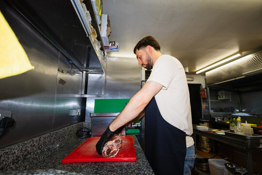 Chef handling a raw lamb rack on a red cutting board