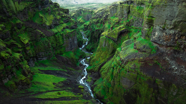 Panoramic aerial view of the lush M&uacute;laglj&uacute;fur Canyon with its hidden waterfall, towering moss-covered cliffs and winding river, one of Iceland's most spectacular natural landscapes.