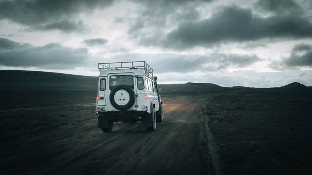 An off-road vehicle drives across the remote volcanic plains near M&aelig;lifell, surrounded by black lava fields, dramatic storm clouds and the rugged beauty of Icelandic Highlands in pristine wilderness.
