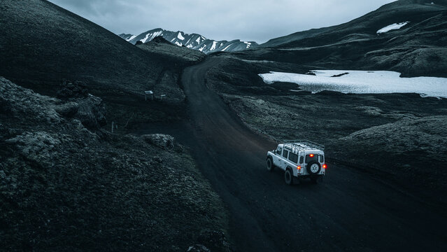 An off-road vehicle travels through the remote volcanic highlands near M&aelig;lifell, surrounded by black lava fields, lingering snow and dramatic mountain scenery in Iceland's untouched wilderness.