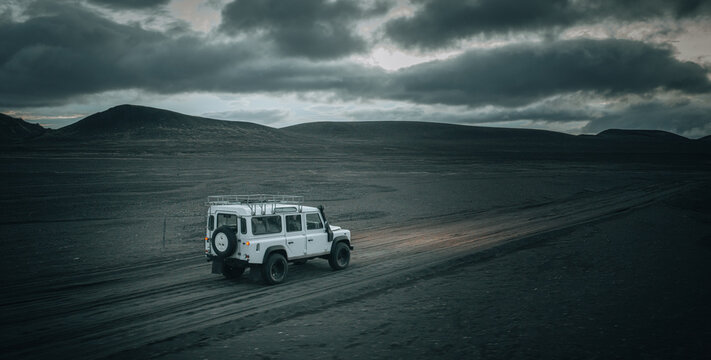 An off-road vehicle drives across the remote volcanic plains near M&aelig;lifell, surrounded by black lava fields, dramatic storm clouds and the rugged beauty of Icelandic Highlands in pristine wilderness.