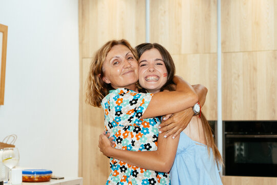 Mother and adult daughter hugging happily in kitchen