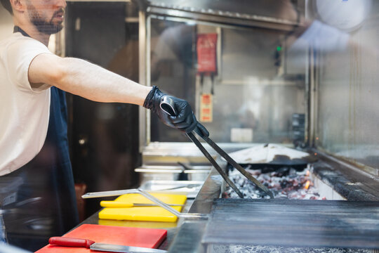 Chef managing hot charcoal embers with tongs at a grill station