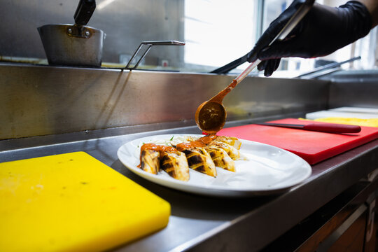 Chef hands pouring hot sauce over a plated Turkish kebab