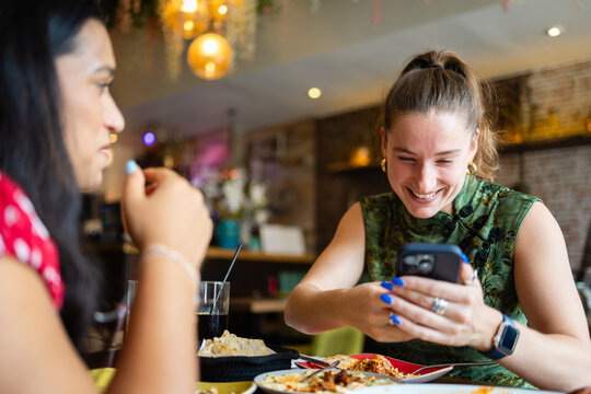 Happy woman checking her phone during a dinner date with a friend