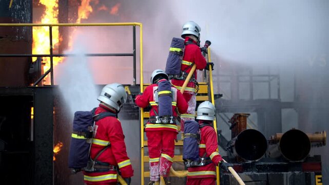 Firefighters work together, climbing ladders to the upper floor with water hoses, during professional firefighting training at an industrial training facility