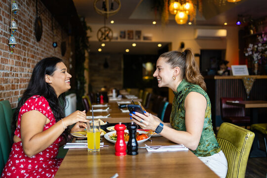 Women laughing while checking a smartphone at a restaurant table