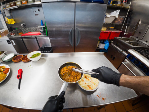 POV of chef spooning meat over hummus