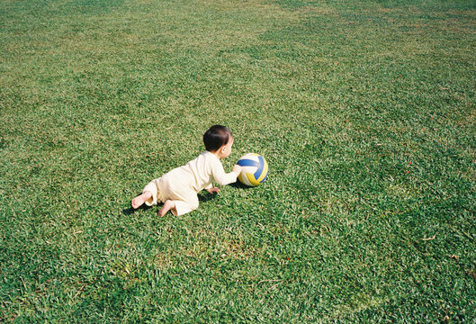 Baby crawling on green grass towards a colorful ball