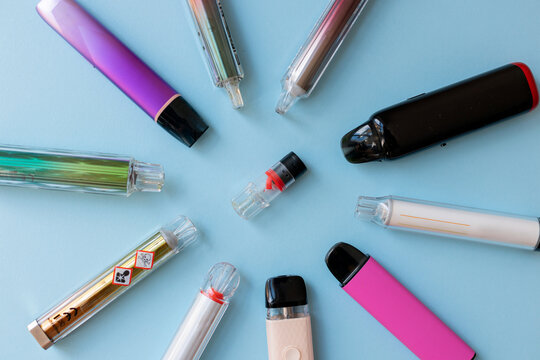 Diverse e-cigarettes arranged in a circle on a blue background, a few with toxic warning symbols. Highlighting harmful effects.