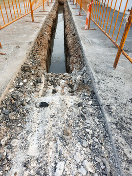 Utility work trench filled with muddy water and lined with metal fences during construction