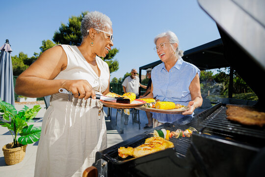 Joyful senior friends grilling barbecue food outdoors