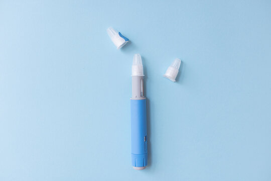 Insulin injection pen with needle caps on blue background. Medical device representing diabetes risks, chronic health complications, metabolic disease, and side effects of medication therapy.