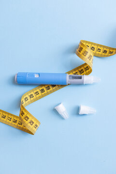 Blue weight loss injection pen with yellow tape measure on light blue background, symbolizing dangerous dieting trends, drug misuse, severe side effects, and obesity health risks.