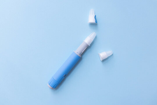 Blue medical injection pen and two removed needle caps on a light blue background. Overhead flat-lay shot. Represents self-medication for chronic conditions.