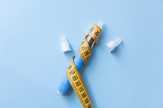 Blue weight loss injection pen wrapped in yellow measuring tape on blue background, conceptualizing risky slimming trends, medication misuse, health hazards, and severe side effects.