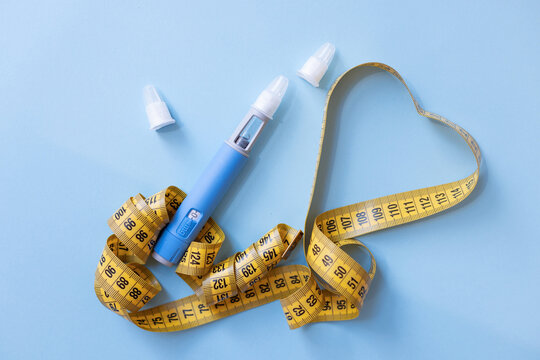 Weight loss injection pen and measuring tape on a blue background. Concept of health risks, dangerous side effects, drug misuse, extreme dieting, and pharmaceutical weight control risks.
