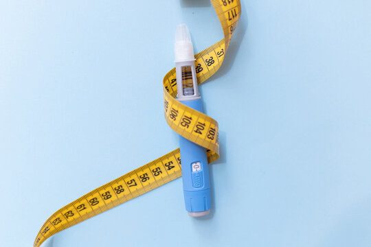 Top view of a medical injection pen tightly wrapped with a yellow measuring tape, symbolizing health risks of rapid weight loss, medication misuse, and dangerous focus on body measurements.