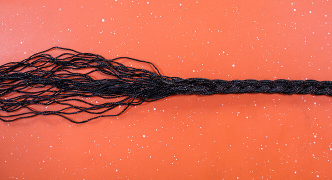 Black braided cord unraveling and fraying at the end illustrating concepts of stress and tension isolated against a bright speckled orange textured background, woven string unraveling into threads