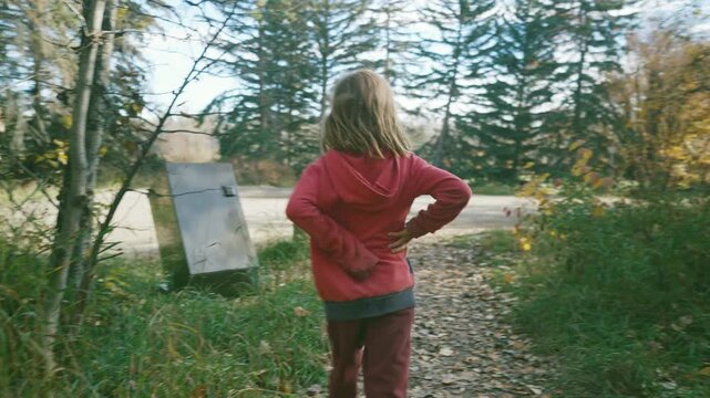 Boy walking out of autumn woods toward a road with spruce trees ahead