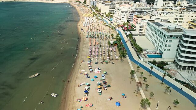 Albania, Durres 07 09 2025: Backward drone video flying along Durres beach showing hotels on right, blue line promenade, umbrella rows, and sea with swimmers on left.