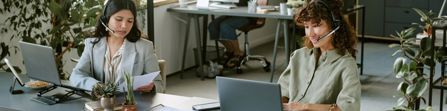 Header of diverse young adult female colleagues wearing headsets working in call center using laptops. Image suitable for customer service, telemarketing, and corporate communication marketing