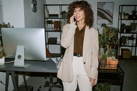 Young adult Biracial woman talking on smartphone in modern office, representing corporate communication. Image suitable for business marketing and remote work advertising, medium shot