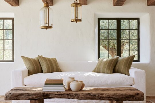 French Provencal farmhouse living room featuring a white sofa with green cushions, rustic wooden coffee table, and large windows with lanterns illuminating the space