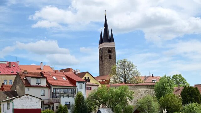 A stone church tower with a dark spire above the red rooftops of an old town, Telc, Czech Republic