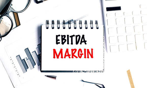 Ebitda margin concept displayed on notebook with financial charts, calculator and eyeglasses for business profitability analysis