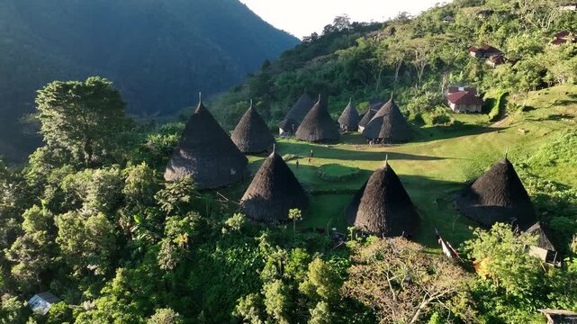 Aerial view of the traditional conical houses of Waerebo Village surrounded by lush tropical mountains in Satar Mese Barat, East Nusa Tenggara, Indonesia.