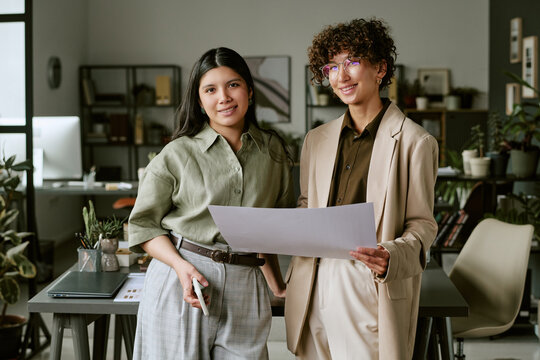 Portrait of diverse young adult female colleagues holding paper document in modern office. Image represents female leadership and teamwork, suitable for corporate communication