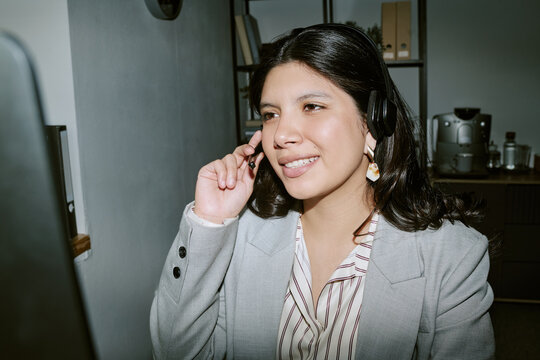 Hispanic young adult female customer service agent working in call center wearing headset. Image ideal for corporate communication, telemarketing, and customer support services