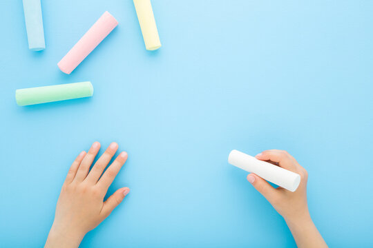 Little child boy hand fingers holding white chalk and writing on light blue table background. Pastel color. Closeup. Empty place for text. Point of view shot. Flat lay. Top down view.