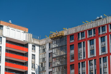 Construction workers operate a scaffold high above a building under renovation on a sunny day © beholdereye