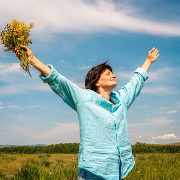 Woman standing in green field with her arms outstretched, facing sun, embracing happiness and beauty of nature. Women's mental health, accepting one's age