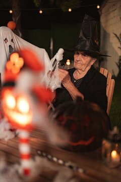 Senior adult woman wearing witch costume holding spider web decoration for Halloween
