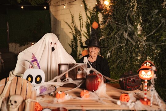 Mature adult woman dressed as a witch with sheet ghost and spooky decorations