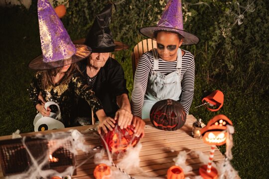 Mixed age range family members wearing witch costumes decorating jack-o-lanterns for Halloween